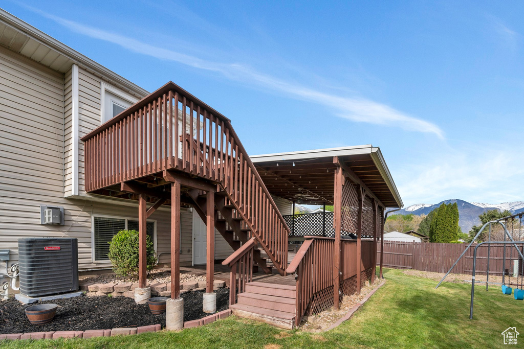 Rear view of house with fence, central AC, a deck with mountain view, a playground, and a yard