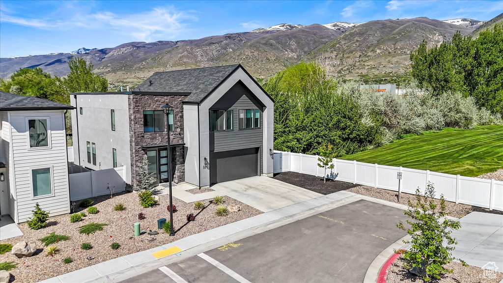View of front of home with a garage, fence, a mountain view, concrete driveway, and stone siding