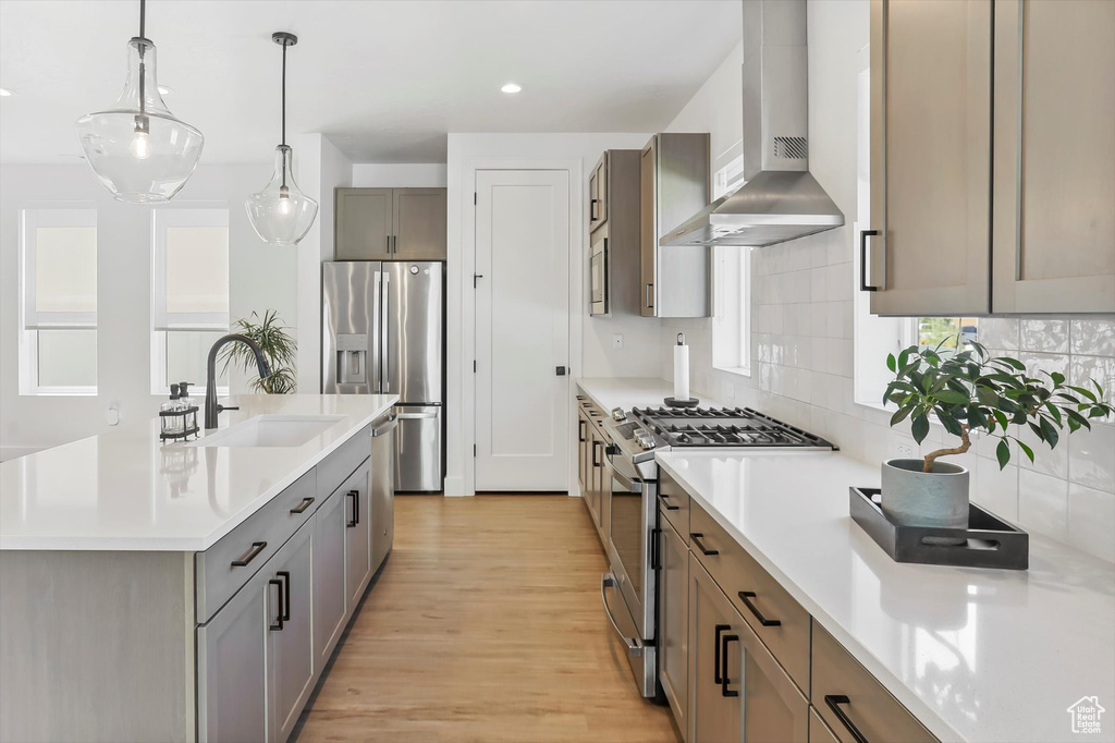 Kitchen featuring a sink, light wood finished floors, light countertops, wall chimney exhaust hood, and stainless steel appliances