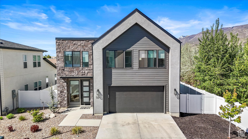 Modern home featuring fence, a gate, driveway, and stone siding