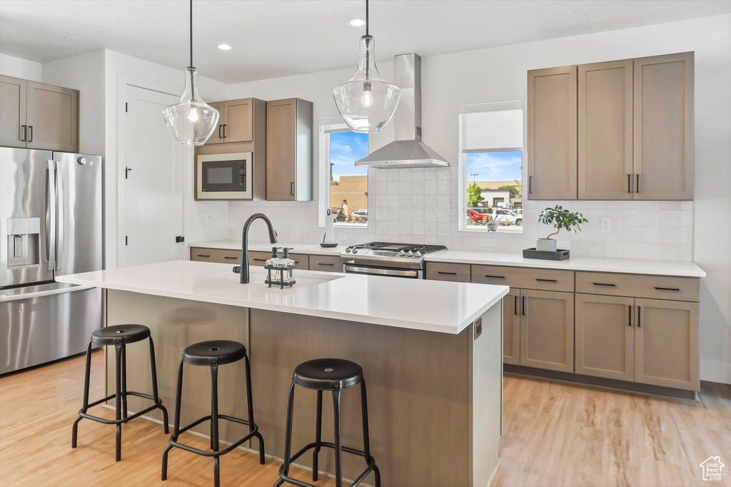 Kitchen with appliances with stainless steel finishes, light wood-type flooring, a sink, a breakfast bar, and wall chimney exhaust hood