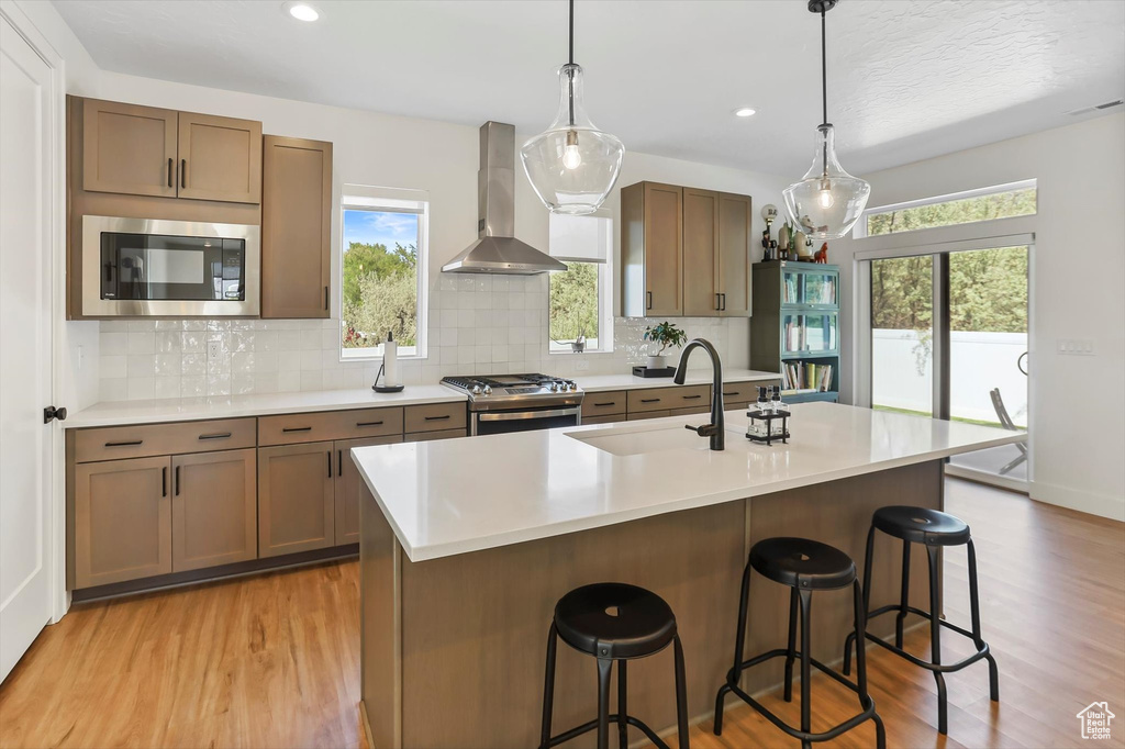 Kitchen featuring wall chimney range hood, light wood-type flooring, light countertops, a sink, and appliances with stainless steel finishes