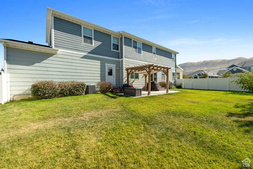 Rear view of house featuring a pergola, a patio, a fenced backyard, a mountain view, and a yard