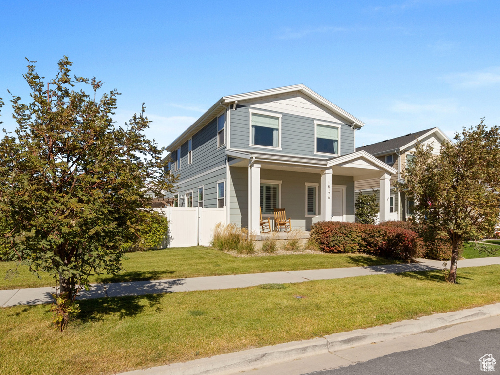View of front of home with covered porch, fence, and a front yard