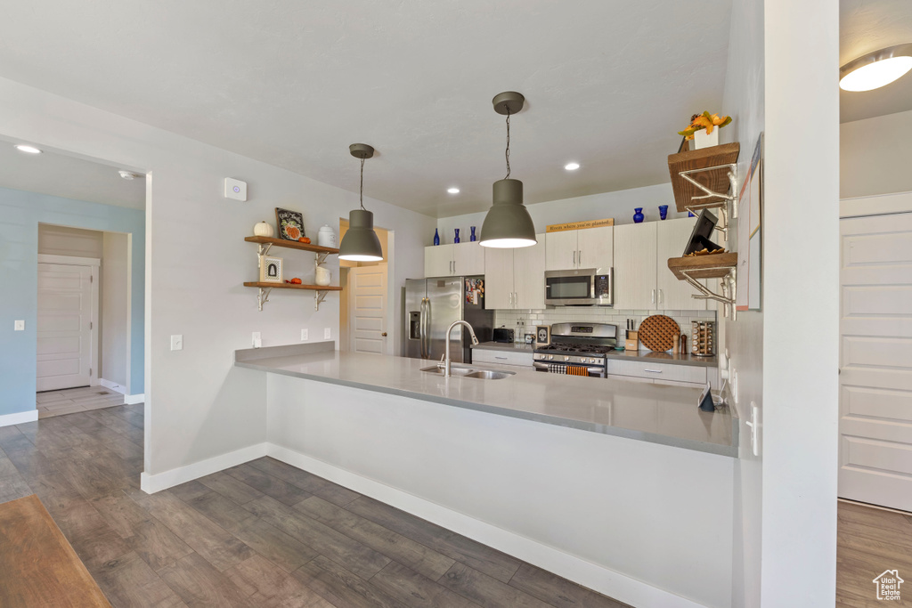 Kitchen featuring open shelves, a sink, stainless steel appliances, a peninsula, and decorative backsplash