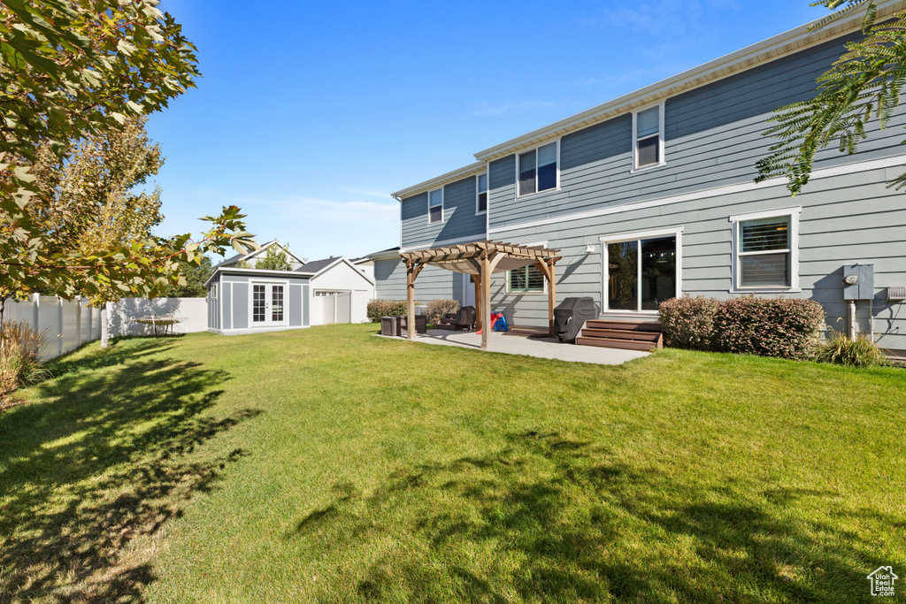 Back of house with an outdoor structure, a pergola, a patio, a fenced backyard, and a yard