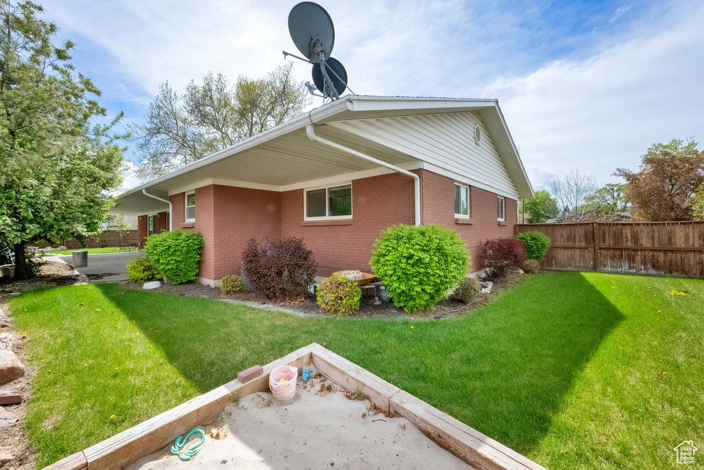 View of property exterior featuring fence, a lawn, and brick siding