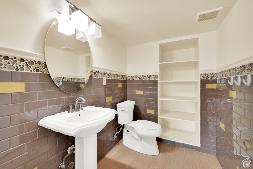 Bathroom featuring tile walls, wainscoting, toilet, and visible vents