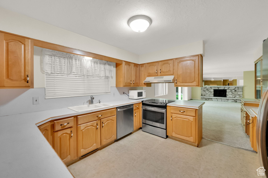 Kitchen featuring appliances with stainless steel finishes, a sink, light countertops, light floors, and under cabinet range hood