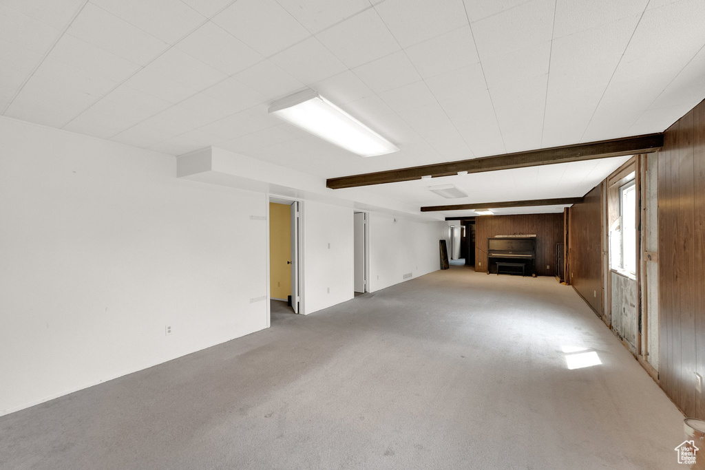 Unfurnished living room with light colored carpet, beam ceiling, wooden walls, and a fireplace