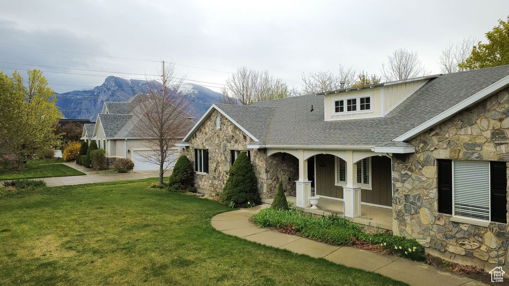 View of front of property with a porch, a front yard, a shingled roof, a mountain view, and stone siding