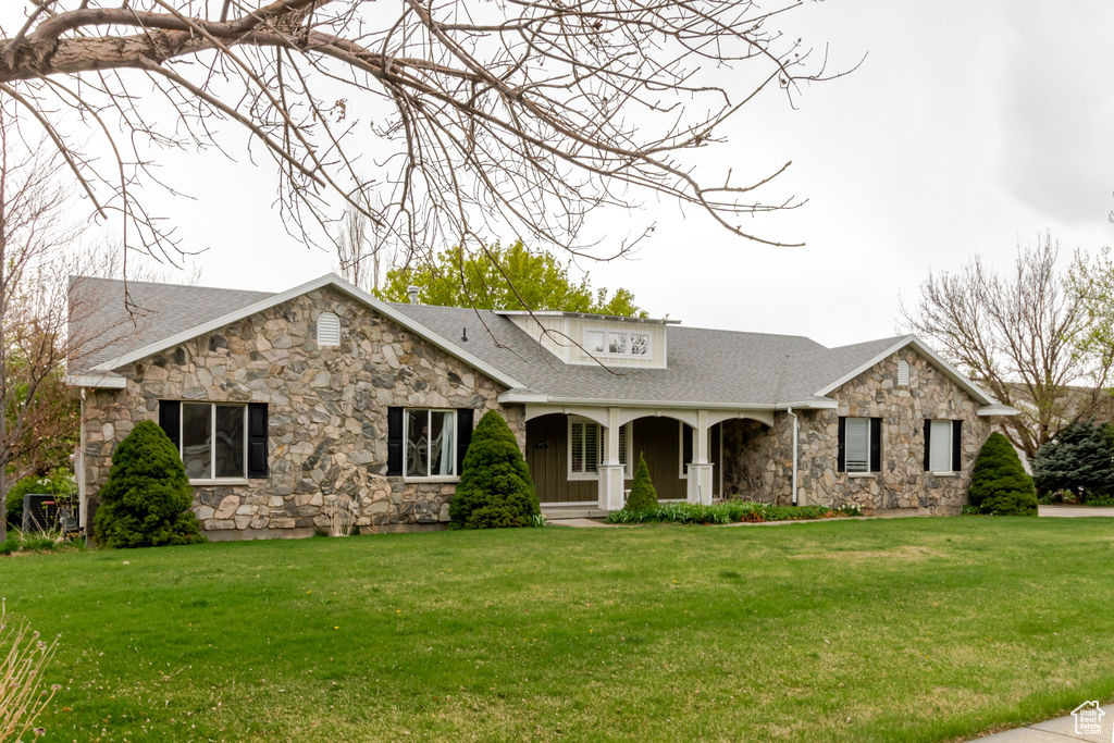 Ranch-style home with a porch, a shingled roof, a front lawn, and stone siding