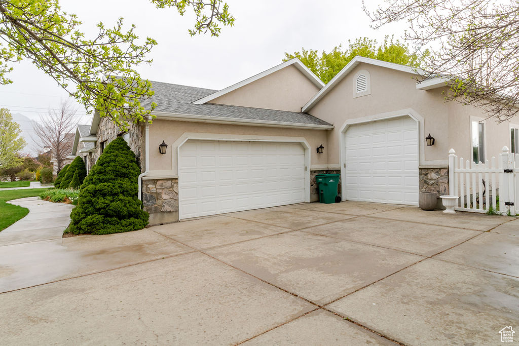 Exterior space featuring an attached garage, concrete driveway, stone siding, and stucco siding