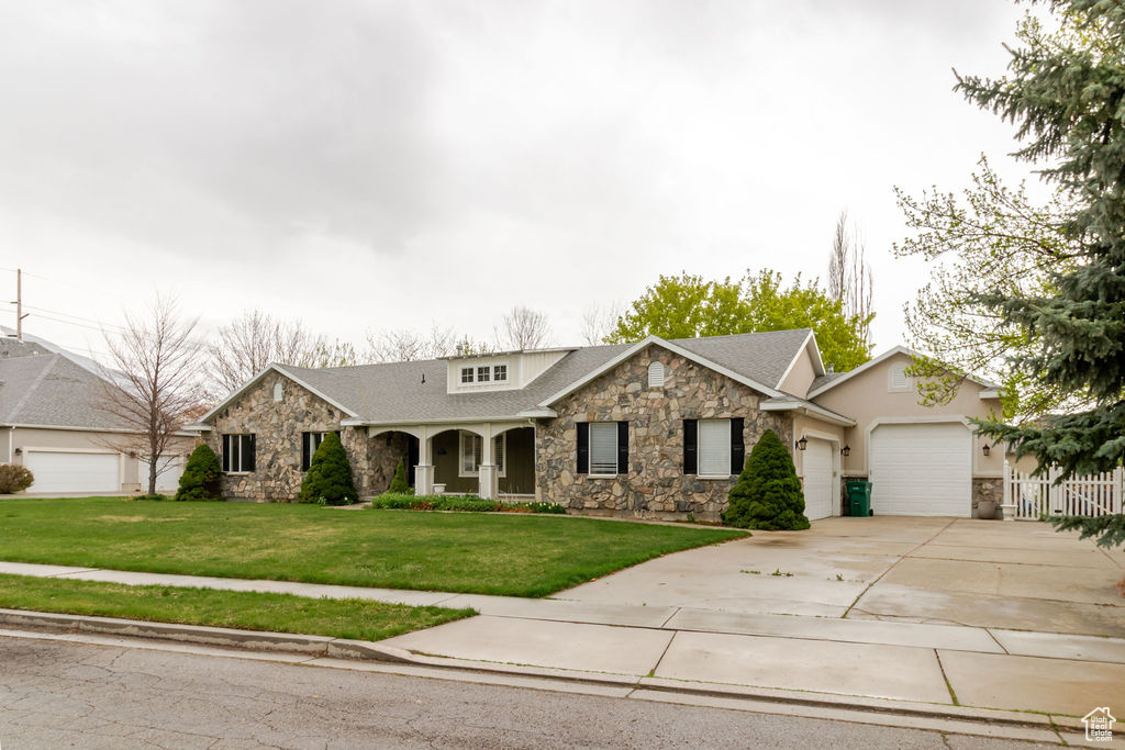 View of front facade with a garage, concrete driveway, a front yard, and stone siding