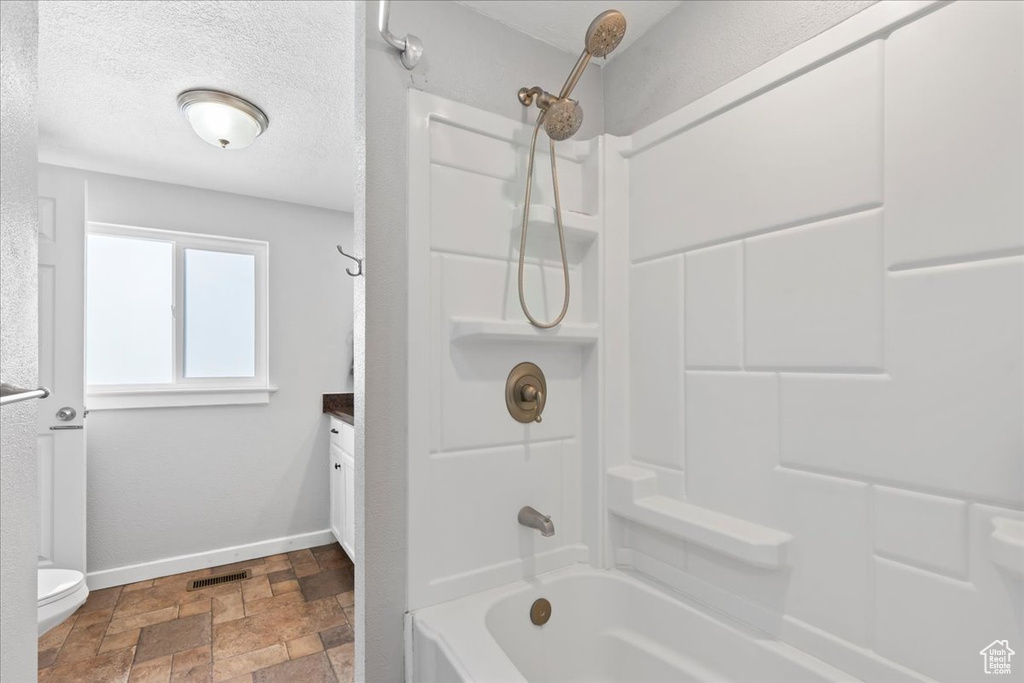 Full bathroom with visible vents, toilet, baseboards, stone finish flooring, and shower / washtub combination