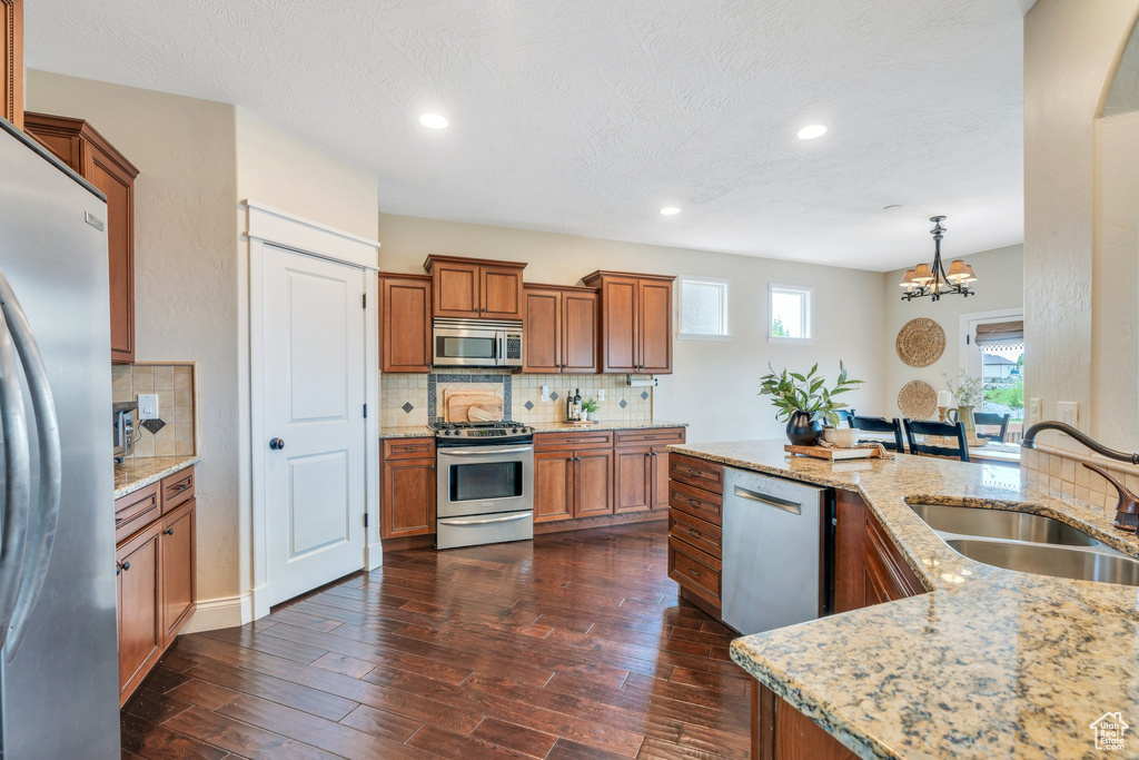 Kitchen featuring brown cabinets, tasteful backsplash, a sink, appliances with stainless steel finishes, and a notable chandelier