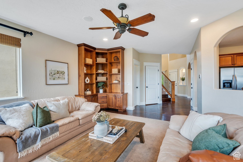 Living room with dark wood-style flooring, arched walkways, stairs, a ceiling fan, and recessed lighting
