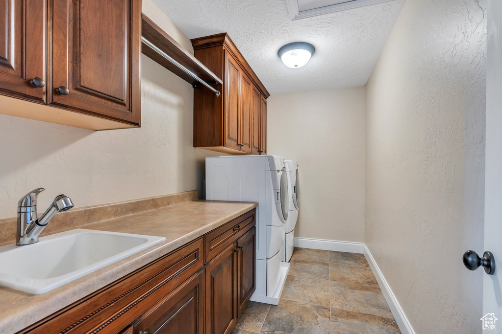 Clothes washing area with washing machine and dryer, baseboards, stone finish flooring, a sink, and cabinet space