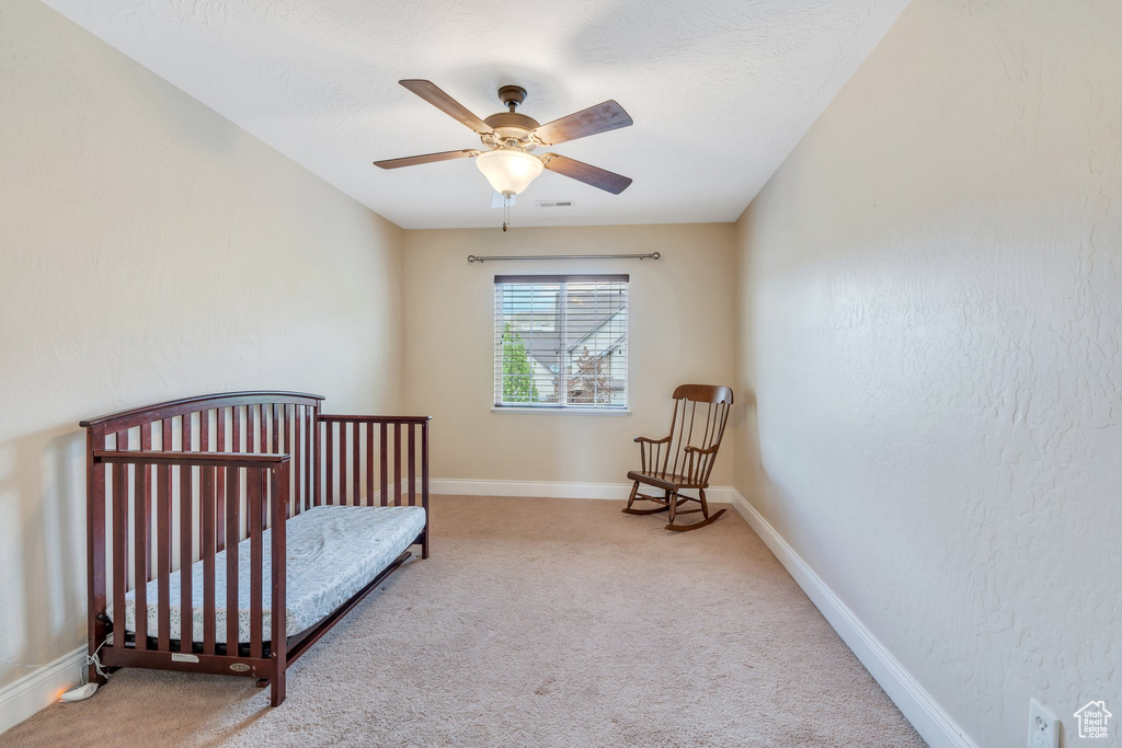 Carpeted bedroom featuring baseboards, a crib, a ceiling fan, and visible vents