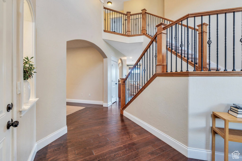 Entryway featuring a towering ceiling, arched walkways, hardwood / wood-style flooring, baseboards, and stairs