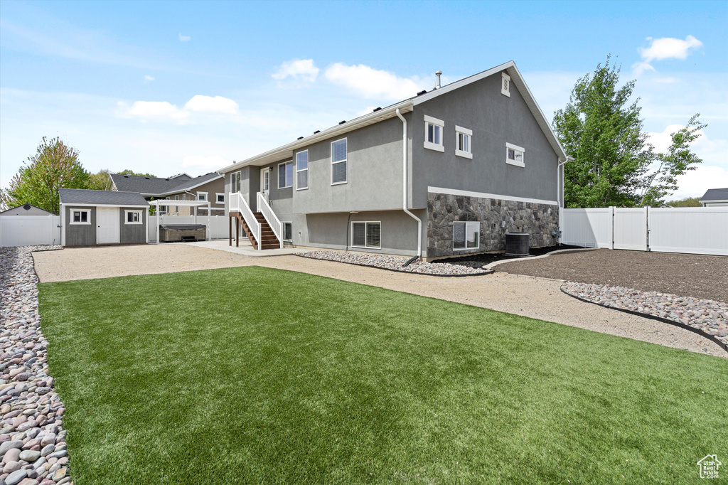 Back of house featuring stone siding, a storage shed, stucco siding, a fenced backyard, and an outdoor structure