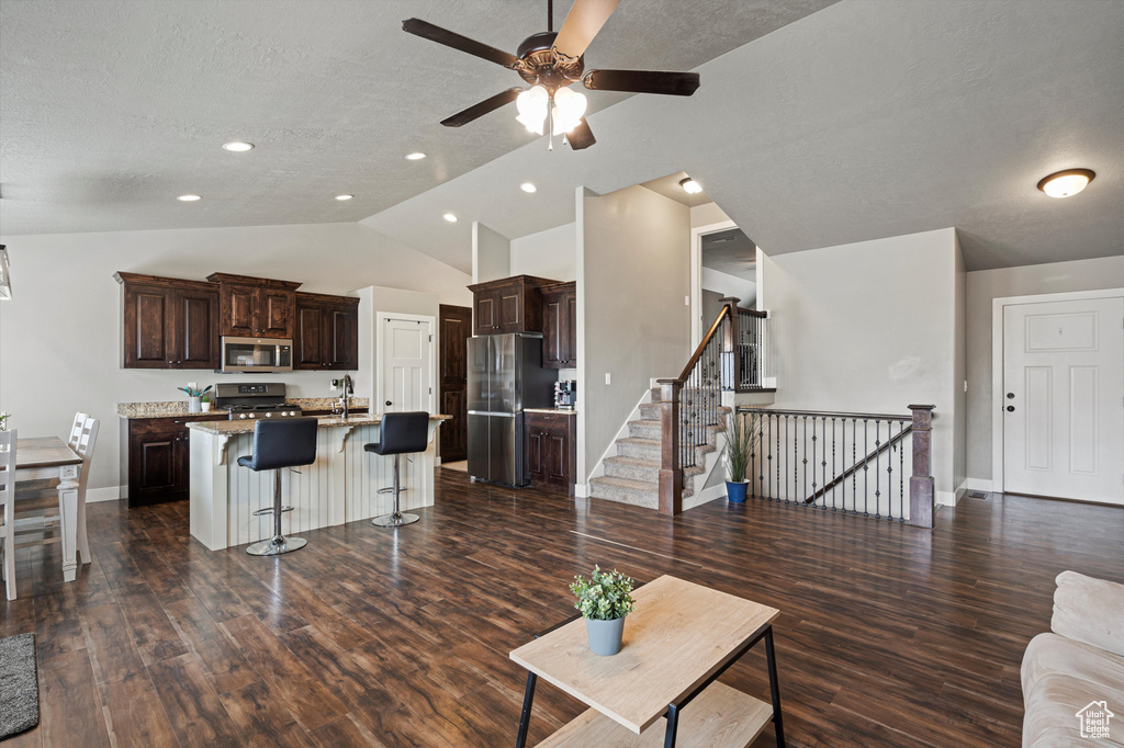 Living room featuring dark wood-style flooring, baseboards, ceiling fan, a textured ceiling, and vaulted ceiling