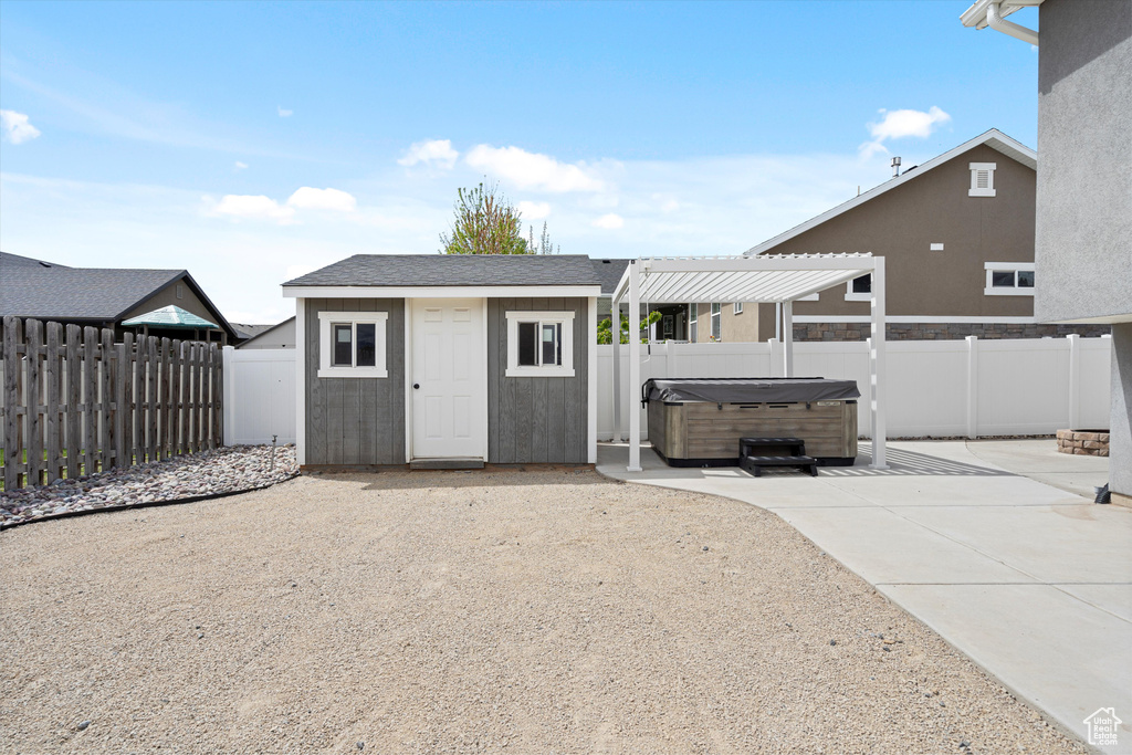 View of outbuilding with a fenced backyard, a hot tub, a pergola, and an outbuilding