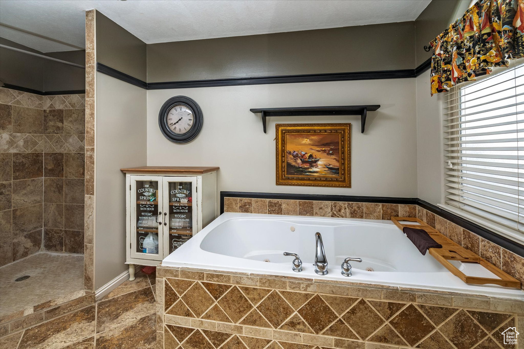 Bathroom with a whirlpool tub, baseboards, stone finish floor, and tiled shower