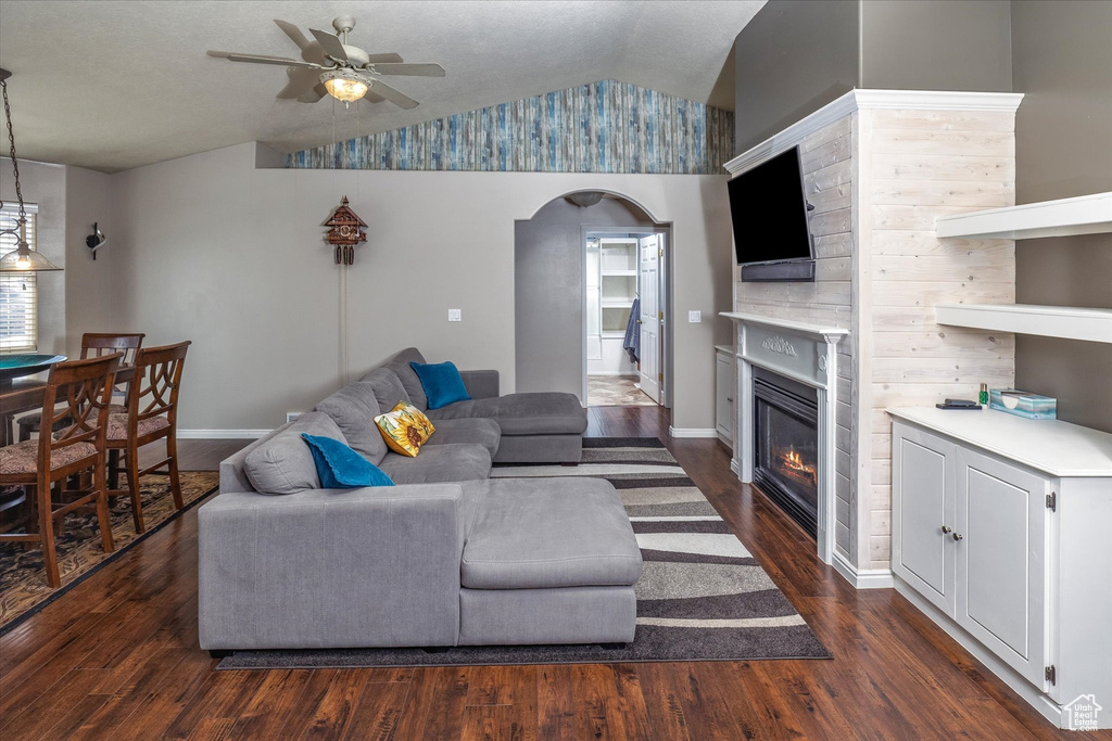 Living room featuring arched walkways, a glass covered fireplace, dark wood finished floors, a ceiling fan, and vaulted ceiling