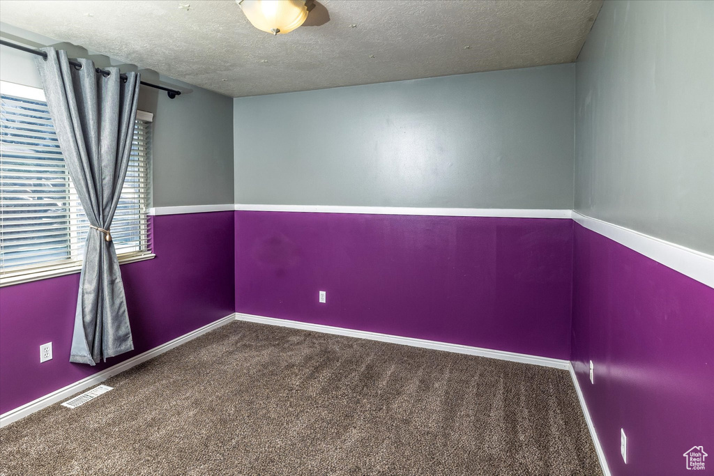 Empty room featuring carpet flooring, a textured ceiling, visible vents, and baseboards