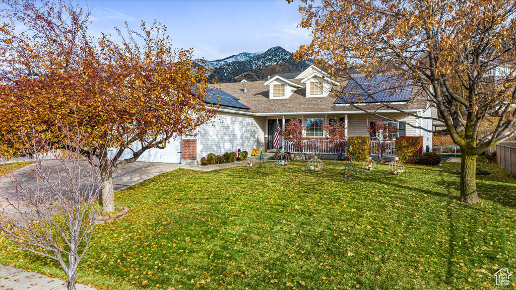 View of front of property with a front lawn, covered porch, a mountain view, driveway, and solar panels