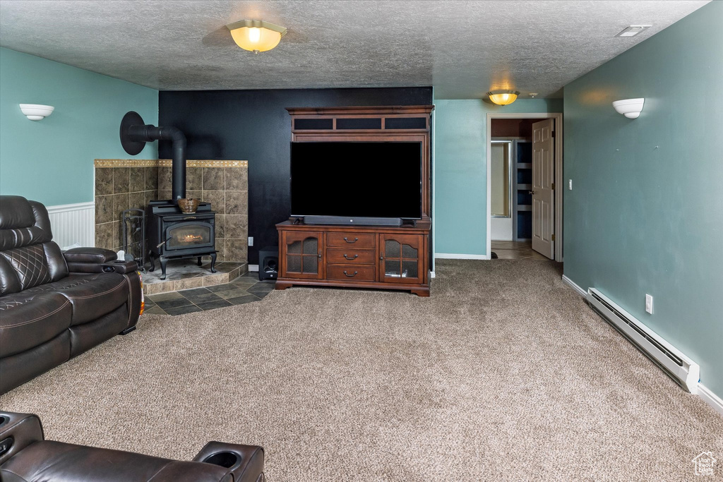 Carpeted living area featuring baseboards, a wood stove, a textured ceiling, and a baseboard heating unit