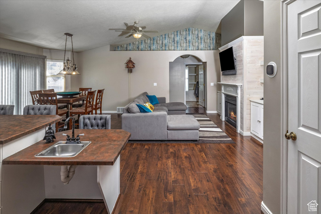 Living room featuring arched walkways, a ceiling fan, dark wood-style floors, and lofted ceiling