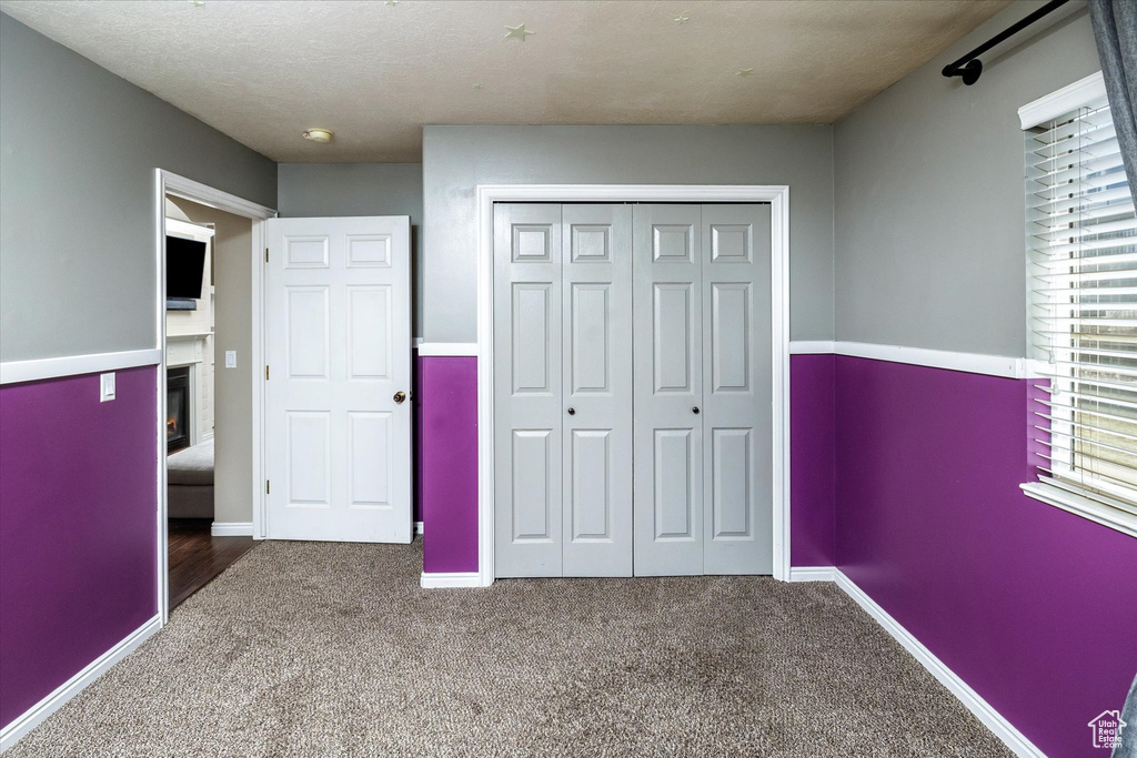 Unfurnished bedroom featuring a glass covered fireplace, baseboards, carpet, and a closet