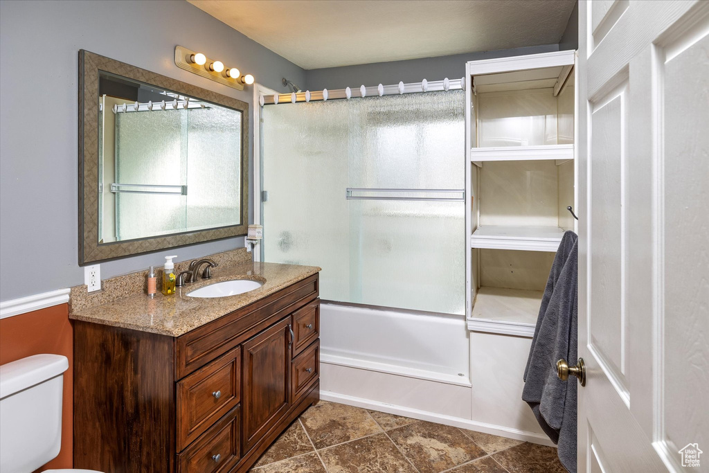 Full bathroom with vanity, bath / shower combo with glass door, tile patterned flooring, and toilet