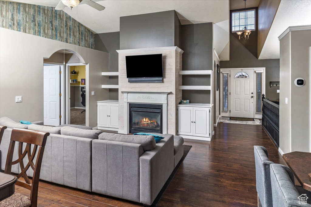 Living room with a glass covered fireplace, high vaulted ceiling, ceiling fan with notable chandelier, and dark wood finished floors