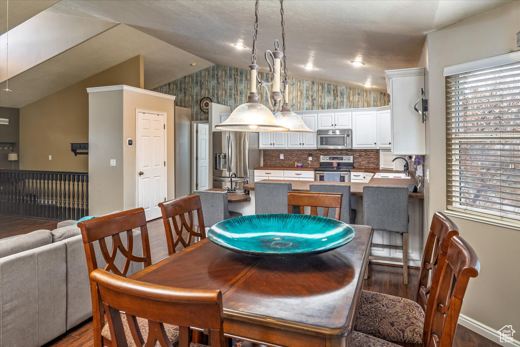 Dining room with wallpapered walls, vaulted ceiling, baseboards, and dark wood-type flooring