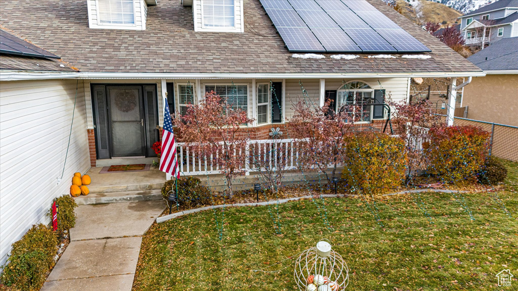 View of exterior entry featuring roof mounted solar panels, roof with shingles, a lawn, and covered porch