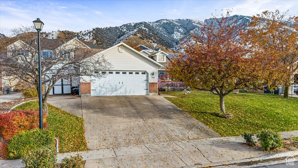 View of front of home with an attached garage, a front lawn, brick siding, a mountain view, and concrete driveway