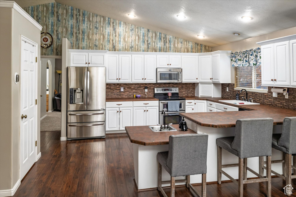 Kitchen featuring dark countertops, appliances with stainless steel finishes, a sink, a peninsula, and wallpapered walls