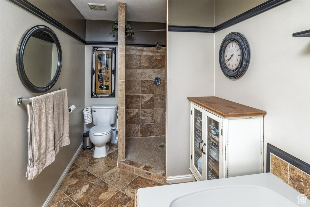 Full bath with baseboards, stone tile floors, visible vents, and toilet