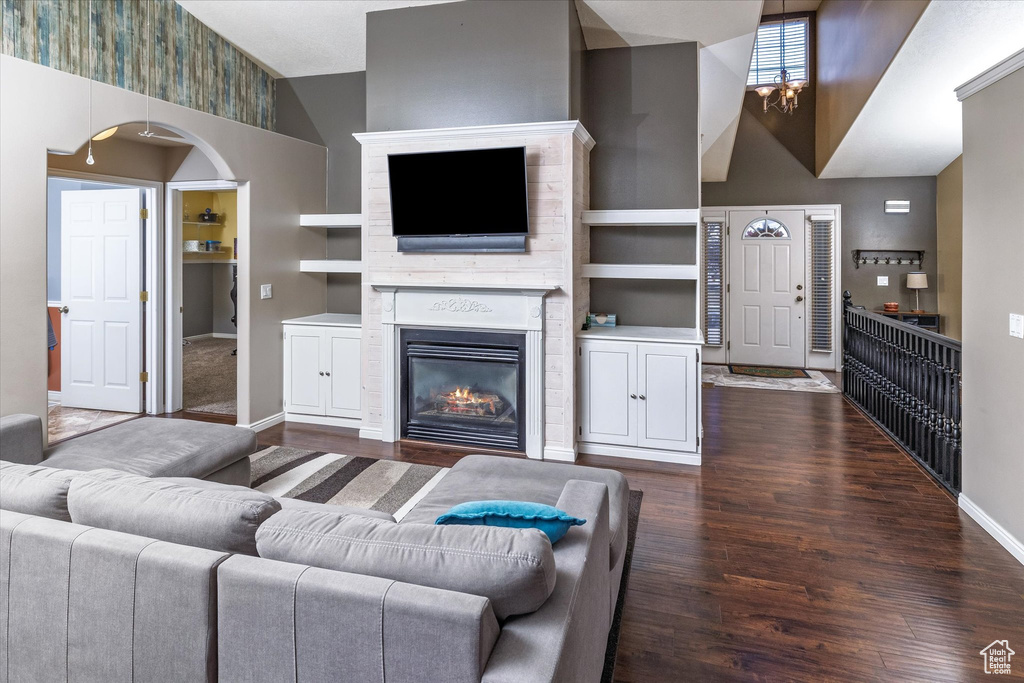 Living room with a towering ceiling, wood finished floors, built in shelves, baseboards, and a glass covered fireplace