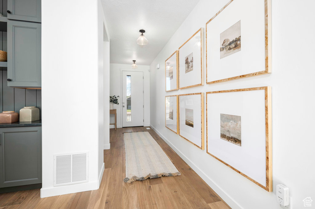 Corridor with baseboards, light wood-type flooring, and visible vents