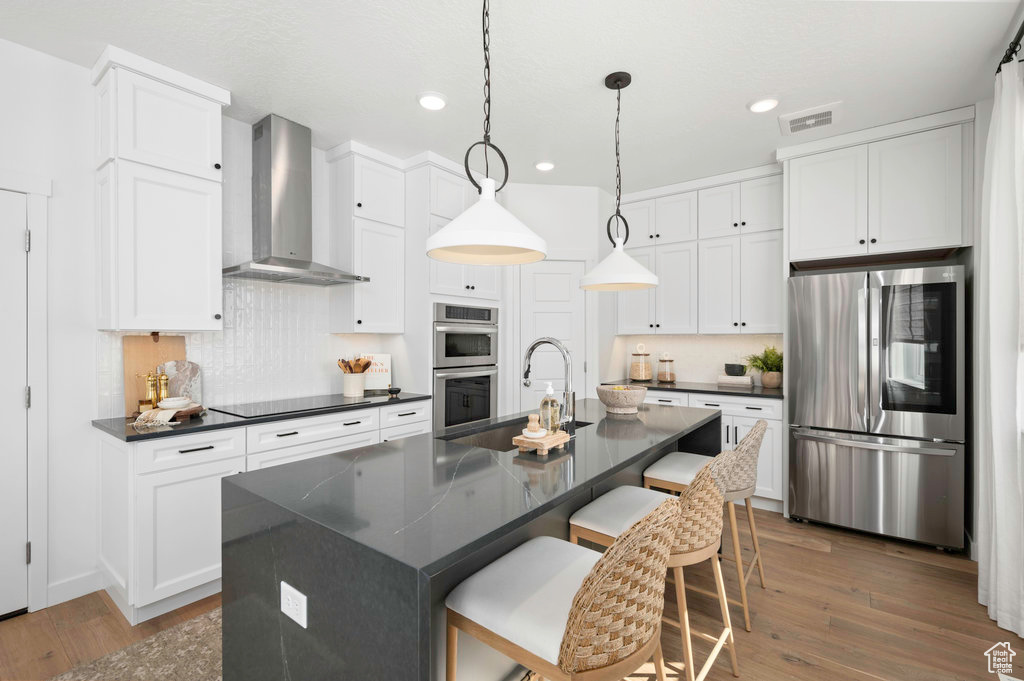 Kitchen with wall chimney range hood, dark countertops, appliances with stainless steel finishes, a sink, and wood-type flooring
