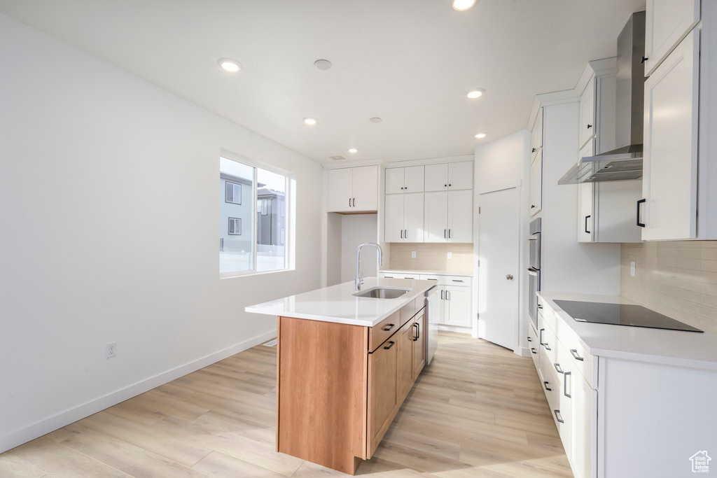 Kitchen with a kitchen island with sink, black electric cooktop, tasteful backsplash, a sink, and light wood finished floors