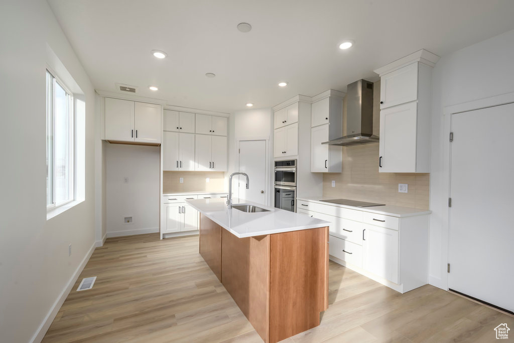 Kitchen with wall chimney range hood, backsplash, visible vents, a sink, and double oven