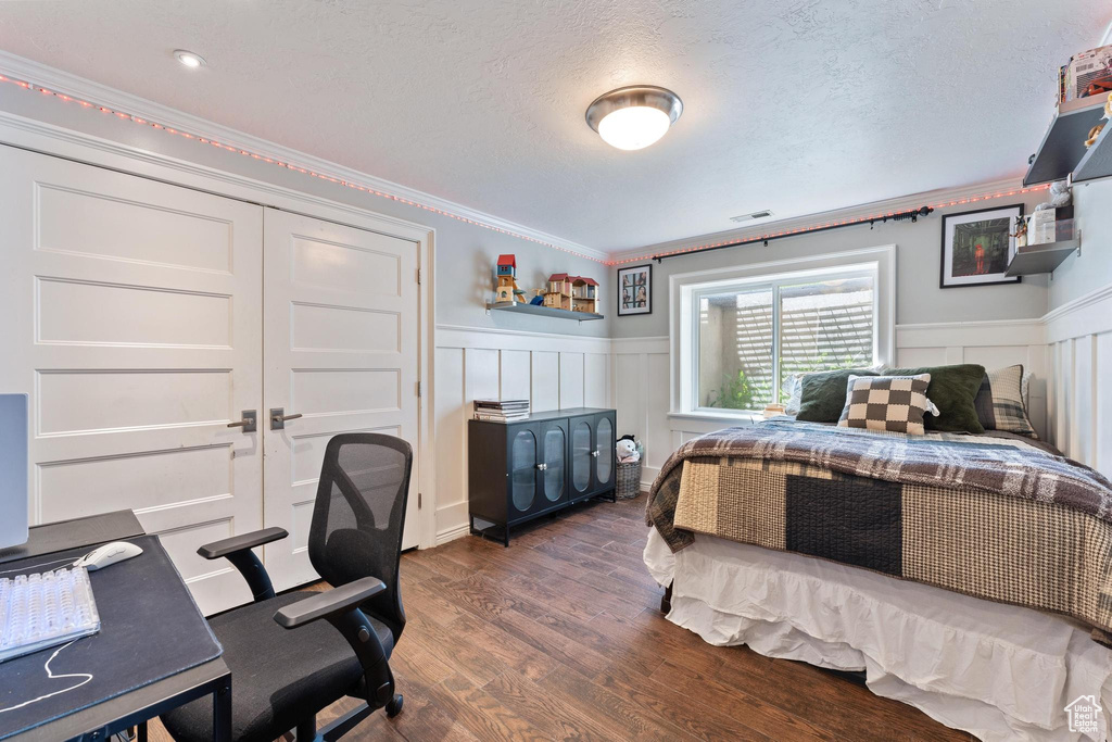 Bedroom featuring ornamental molding, a decorative wall, wood finished floors, a textured ceiling, and a wainscoted wall