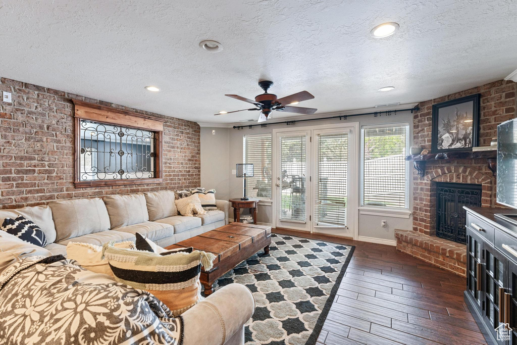 Living room featuring a ceiling fan, a textured ceiling, dark wood-style flooring, and a fireplace