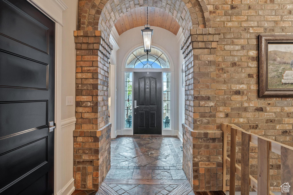 Foyer entrance featuring brick wall, baseboards, vaulted ceiling, and stone tile flooring