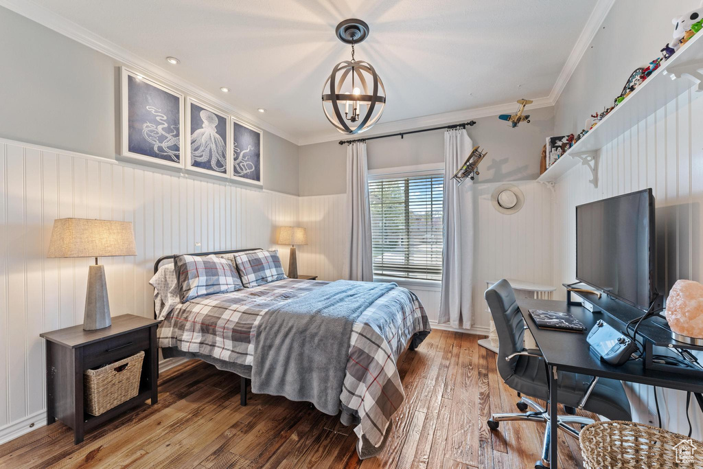 Bedroom featuring an inviting chandelier, a wainscoted wall, crown molding, and wood-type flooring